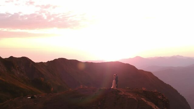 A wedding at the very top of the mountain. Amazing view a young bride in a white wedding dress and veil standing on a rock against the backdrop of mountains and sunset