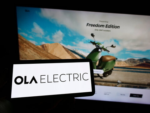 Stuttgart, Germany - 08-27-2022: Person holding mobile phone with logo of Indian company Ola Electric Mobility Pvt. Ltd. on screen in front of web page. Focus on phone display.