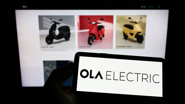 Stuttgart, Germany - 08-27-2022: Person holding cellphone with logo of Indian company Ola Electric Mobility Pvt. Ltd. on screen in front of webpage. Focus on phone display.