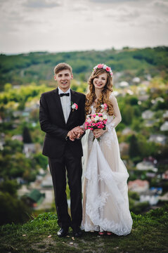 Romantic couple newlyweds, bride and groom stands and holding bouquet of pink flowers and greens, greenery in the country. Wedding ceremony on nature.