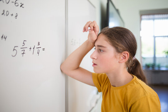 teenager child student thinks over solves example problem with fractions on blackboard in school classroom in math algebra lesson. on face is bright emotion of surprise, difficulty, thoughts