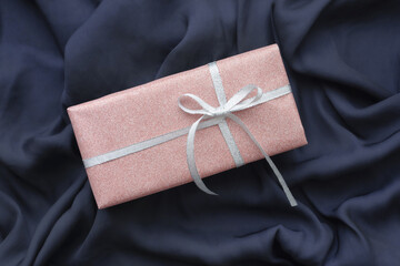 Present in pink lame wrapping placed on navy semi-glossy cloth