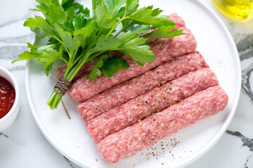 Closeup of raw serbian cevapi or cevapcici sausages with fresh parsley on a white plate, selective focus, horizontal shot