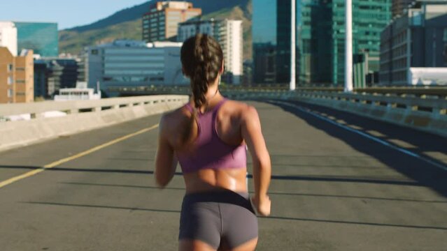 Fitness woman, city runner and training on a road of an urban bridge for a cardio workout from behind. Sport motivation and athletic exercise while running for a healthy, strong and fit sports body