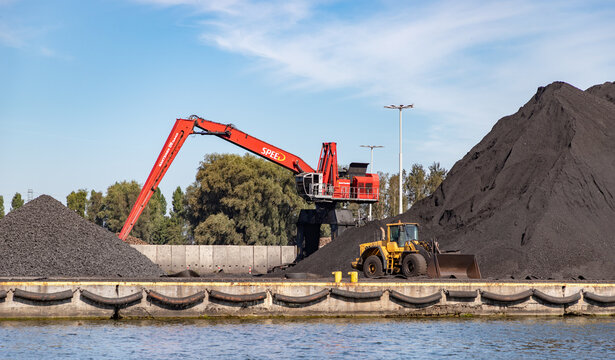 Gdansk, Poland - August 14, 2022: A picture of a crane and a bulldozer next to large piles of gravel and coal in the Gdansk Shipyard.