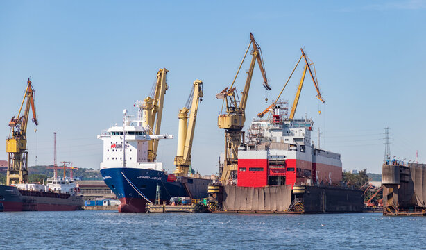 Gdansk, Poland - August 14, 2022: A picture of a vessel being repaired next to large cranes, as well as a docked one, in the Gdansk Shipyard.