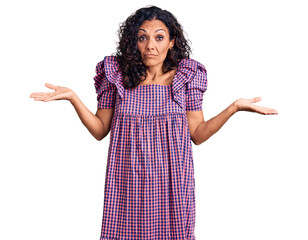 Middle age beautiful woman wearing casual dress clueless and confused expression with arms and...