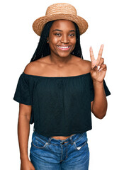 Young african american woman wearing summer hat smiling with happy face winking at the camera doing victory sign. number two.