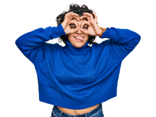 Young hispanic woman with curly hair wearing turtleneck sweater doing ok gesture like binoculars sticking tongue out, eyes looking through fingers. crazy expression.