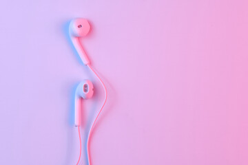 Wired white earphones isolated on white background close-up in pink neon light