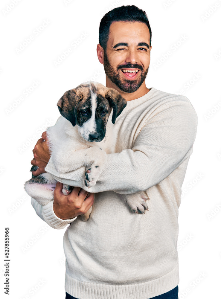 Poster Young hispanic man with beard hugging cute dog winking looking at the camera with sexy expression, cheerful and happy face.