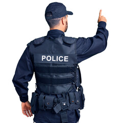 Young hispanic man wearing police uniform posing backwards pointing ahead with finger hand