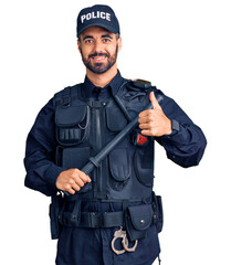 Young hispanic man wearing police uniform holding baton smiling happy and positive, thumb up doing excellent and approval sign