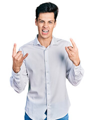 Fototapeta premium Young hispanic business man wearing business clothes shouting with crazy expression doing rock symbol with hands up. music star. heavy concept.