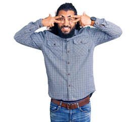 Young arab man wearing casual clothes doing peace symbol with fingers over face, smiling cheerful showing victory