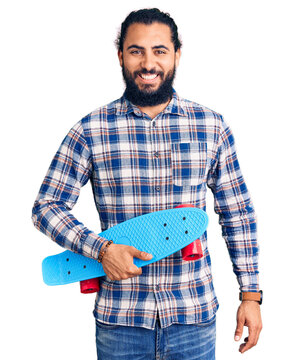 Young arab man holding skate looking positive and happy standing and smiling with a confident smile showing teeth