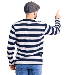 Young handsome man wearing burglar mask posing backwards pointing ahead with finger hand