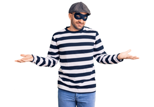 Young handsome man wearing burglar mask smiling showing both hands open palms, presenting and advertising comparison and balance - Powered by Adobe