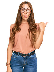 Young hispanic woman wearing casual clothes and glasses surprised pointing with hand finger to the...