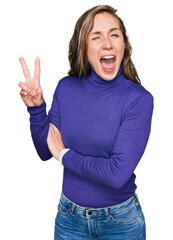 Young blonde woman wearing casual clothes smiling with happy face winking at the camera doing victory sign. number two.