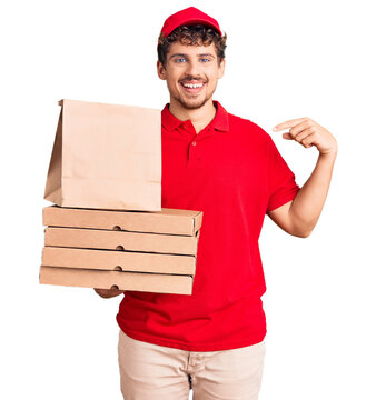 Young handsome man with curly hair holding delivery pizza box pointing finger to one self smiling happy and proud