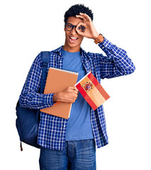 Young african american man wearing student backpack holding spanish flag smiling happy doing ok sign with hand on eye looking through fingers