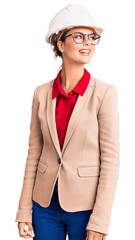 Young beautiful woman wearing architect hardhat looking away to side with smile on face, natural expression. laughing confident.