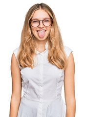 Beautiful young caucasian girl wearing casual clothes and glasses sticking tongue out happy with funny expression. emotion concept.
