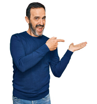 Middle age hispanic man wearing casual clothes amazed and smiling to the camera while presenting with hand and pointing with finger.