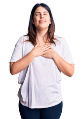 Young beautiful brunette woman wearing casual t-shirt smiling with hands on chest with closed eyes and grateful gesture on face. health concept.