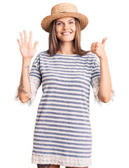 Obraz na płótnie Canvas Beautiful caucasian woman wearing summer hat showing and pointing up with fingers number six while smiling confident and happy.