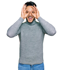 Young arab man wearing casual clothes doing ok gesture like binoculars sticking tongue out, eyes looking through fingers. crazy expression.