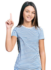 Young brunette girl with long hair wearing casual striped t shirt smiling with an idea or question pointing finger up with happy face, number one
