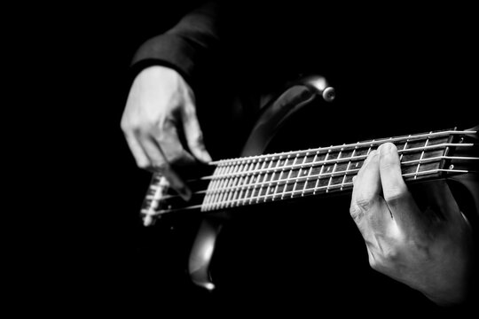 black and white musician hands playing electric bass guitar on black background. music concept