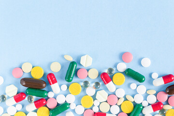 Pills of different shapes and colors are scattered on a blue background