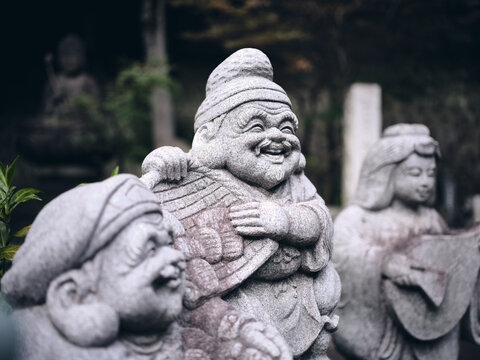 stone statue of laughing Ebisu, one of the japanese seven lucky gods in a quiet temple of tokyo with a dark background
