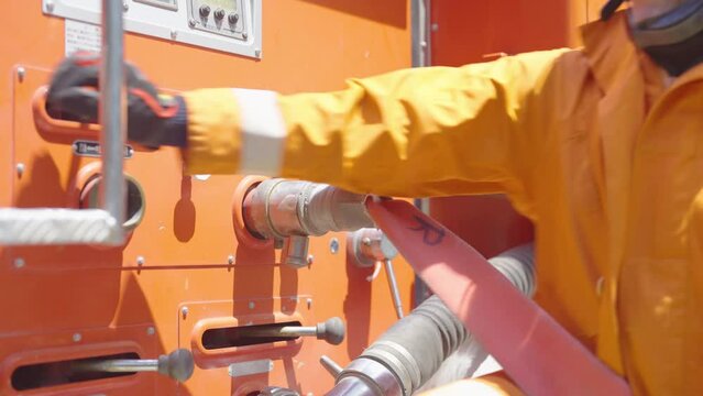 Close up hands of fireman or firefighter control attach fire head pipe then release water using control panel at side of fire truck.