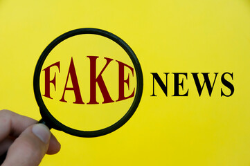 Close-up at fake news text through magnifying glass on yellow cover background. Fake news concept