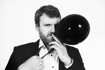 A portrait of a handsome man blowing up a black balloon like a cigarette and tugging at his tie