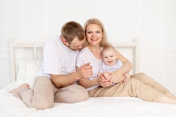happy family mom, dad and baby play on the bed at home and have fun
