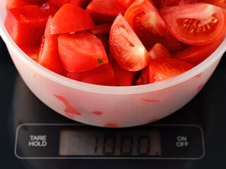 A bowl with kilogram of tomato slices on a digital scale. Focus is on tomatoes - obrazy, fototapety, plakaty