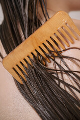 Closeup of female back with wet hair strands covered with conditioner and wooden comb,