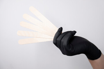 A woman's hand in a glove holds wooden spatulas for wax and sugar depilation. Depilation materials