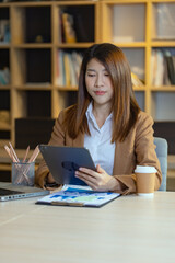 Happy asian young businesswoman using laptop with business finance chart sitting at office working space, Business finance and accounting woman concept.