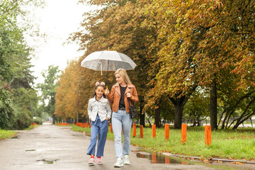 Cheerful mother and her little daughter having fun together in the autumn background under the umbrella. Happy family in the fall background
