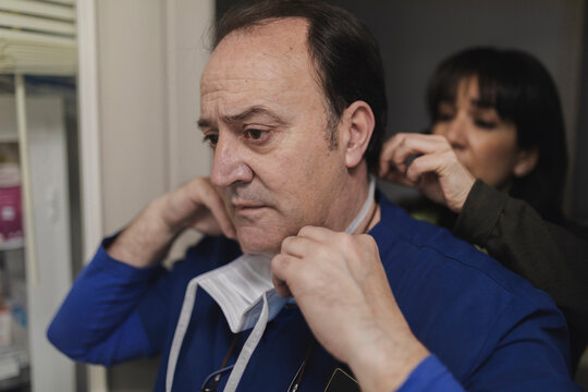 Woman Helping Doctor In Uniform Putting On Mask