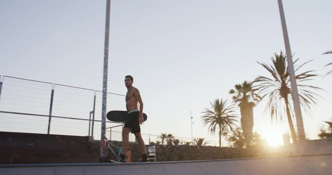 Young athletic shirtless skater walk on edge of pool at sunset. Cool millennial generation activity or sport. Cinematic skating lifestyle vibes. 