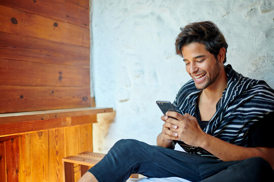 Stylish Hispanic man chatting on smartphone on bed