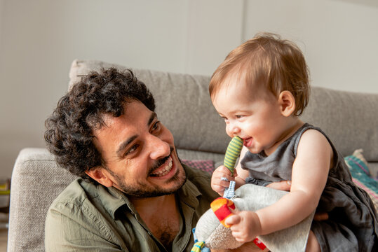 Cheerful young ethnic father playing with curious baby at home