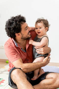 Joyful young father with baby playing together with toys sitting on mat